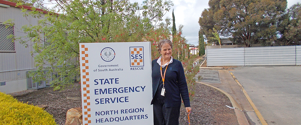 Sign outside the SA State Emergency Service North Region headquarters with an SES staff member standing beside it